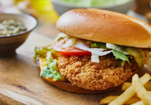 Crispy chicken burger with French fries, salad and tomato, served  in cafeteria, bar, restaurant or home,  table background, close up view with copy space, representing street food, fast food and city life, indulgence and joy through gourmet lifestyle