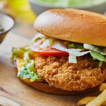 Crispy chicken burger with French fries, salad and tomato, served  in cafeteria, bar, restaurant or home,  table background, close up view with copy space, representing street food, fast food and city life, indulgence and joy through gourmet lifestyle